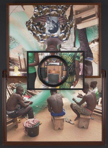 four separate colored photographs layered over each other and attached with black tape on the back; bottom photograph depicts four boys, seated, weaving a fishing net; boy on left turns to look at viewer; brown frame with beaded inner edging; top photograph image of figure in a patterned dress, holding a black and white portrait with both hands; face is obstructed by another photograph layered on top of the image; two figures stand behind front figure, with cascading fishing nets in the background; brown frame; center photograph depicts the torsos of three figures, right figure wearing a green and yellow tie dyed dress, holding a black purse; center figure wearing a white striped patterned button up shirt with matching pants; left figure wearing a green cotton shirt with black bottoms; image obstructed by center photograph overlapping; center photograph is round in shape, with an interior view of a televisions surrounded by electronic equipment on shelving; stuffed bears rest on shelves around television; rectangular gold trophy/ award rests on top of the television; cleat taped to back of installation